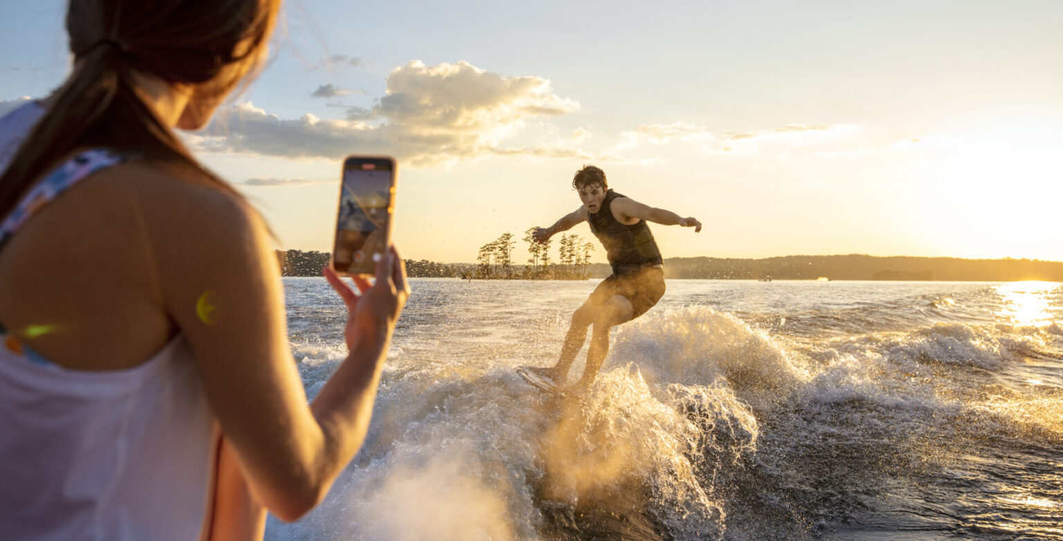 A woman takes a snapshot of a man wakeboarding