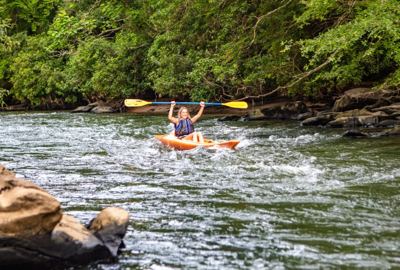 A woman in a kayak holds her paddle over her head triumphantly