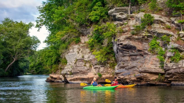 Two kayakers float past a rocky outcropping